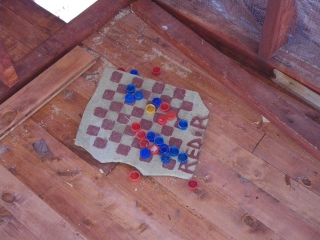 The guys have made a checker board out of mazzera stone and soda bottle lids. They play during lunch.